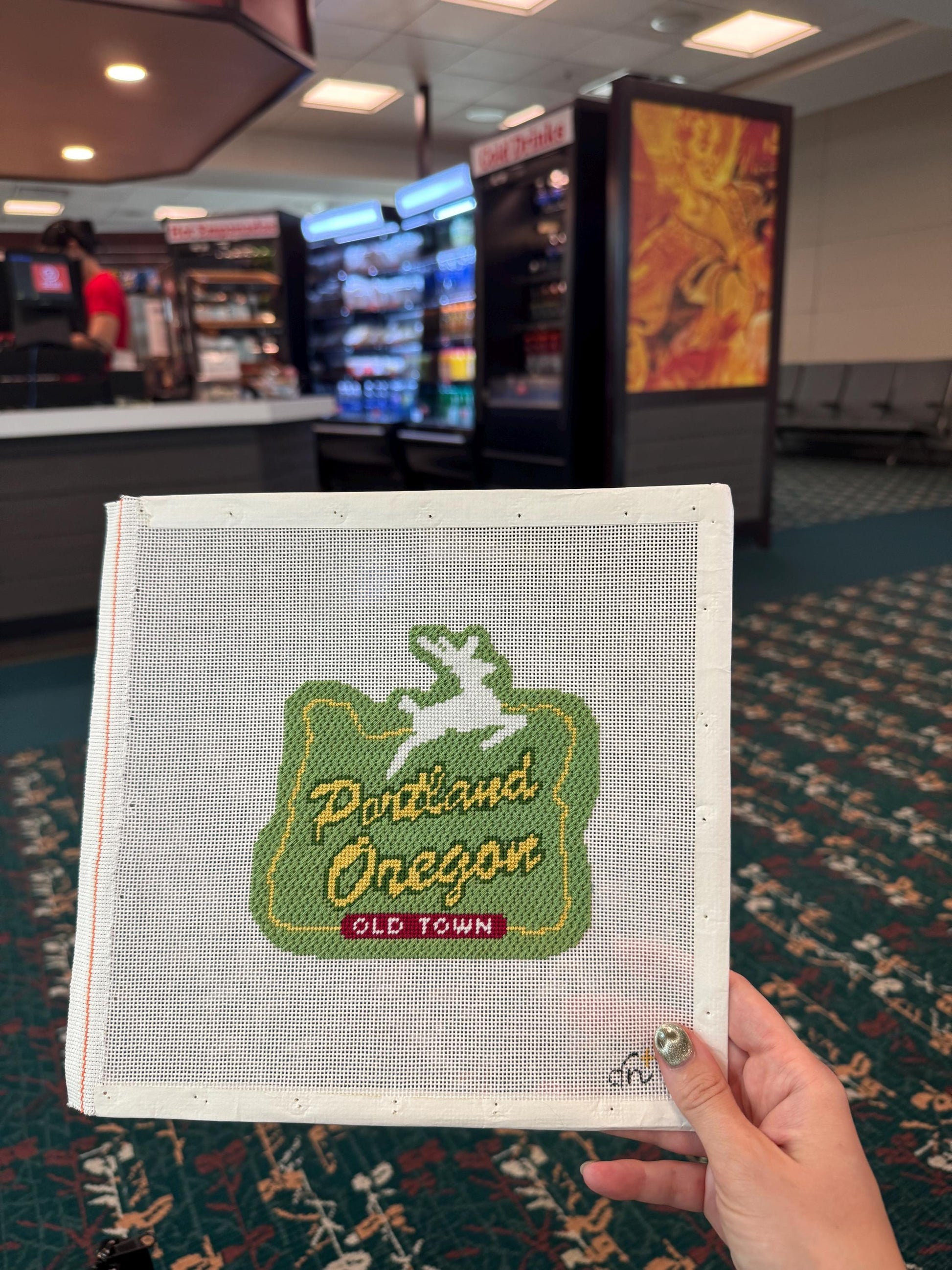 Needlepoint canvas of the Portland Stag shown fully stitched, with a green organic background.